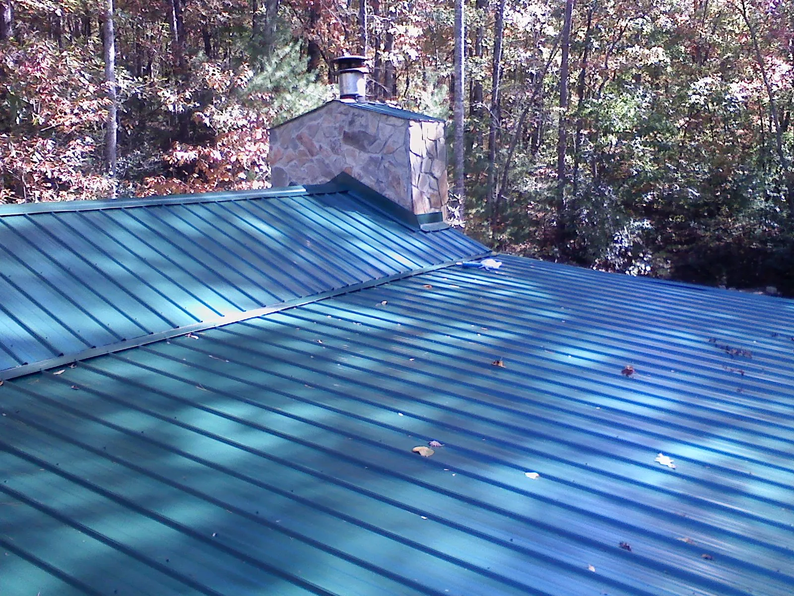 New green metal roof and stone chimney surrounded by autumn woods in Bethany
